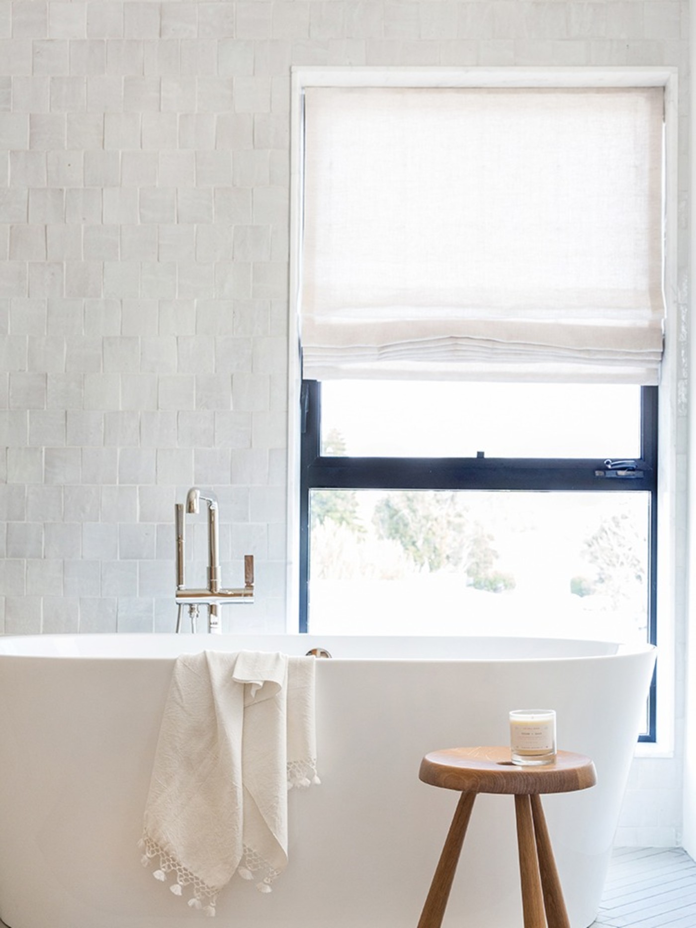 a white bathroom with a wooden stool and a window.