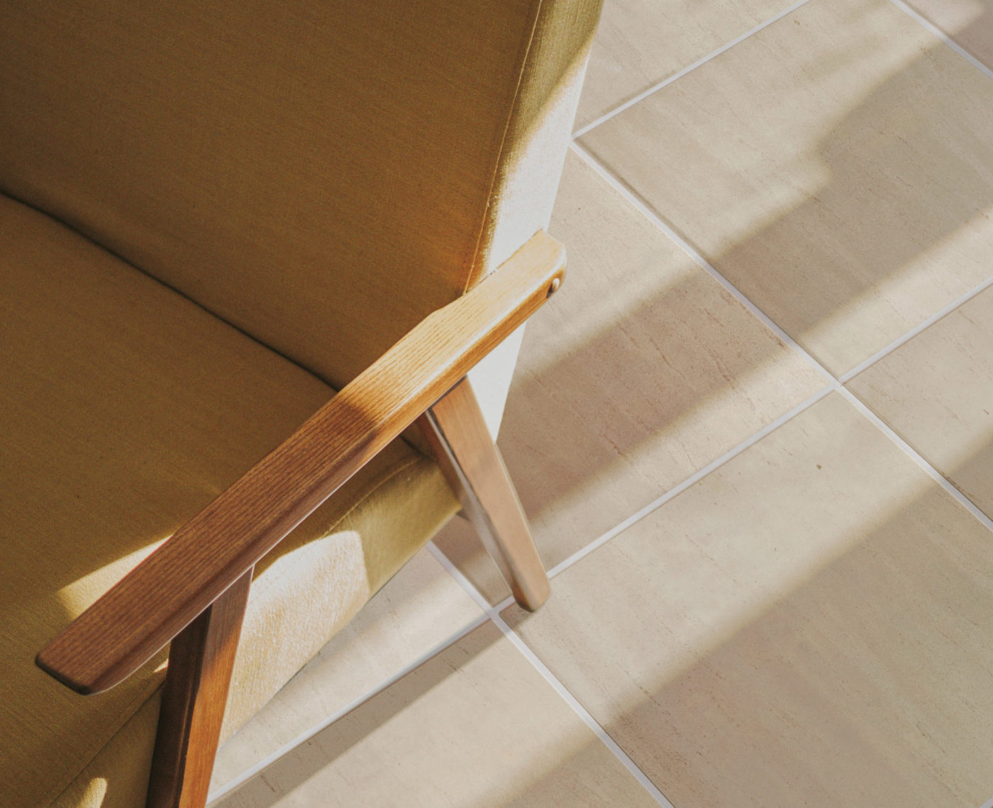 a chair with a wooden arm resting on a tiled floor.