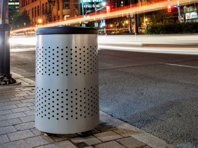 metal triple stream trash and recycling container sitting outside against a red brick wall on a city sidewalk