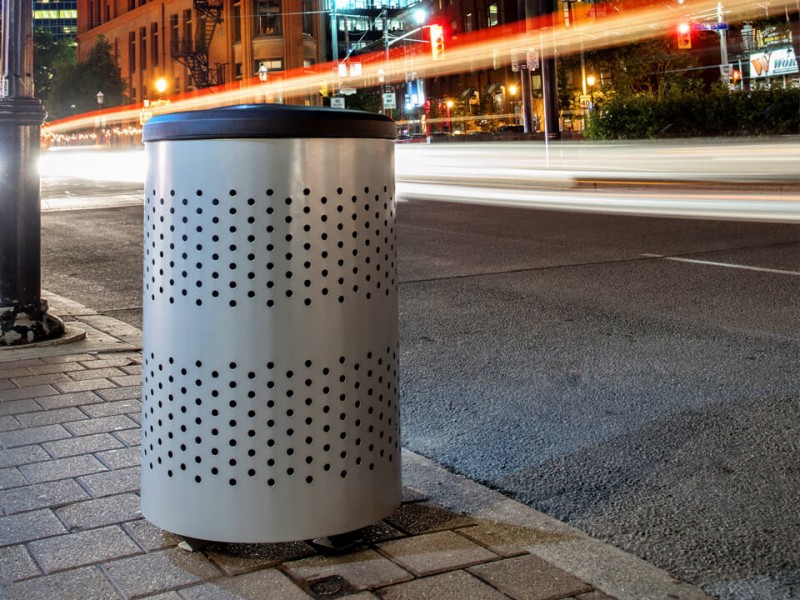 metal triple stream trash and recycling container sitting outside against a red brick wall on a city sidewalk