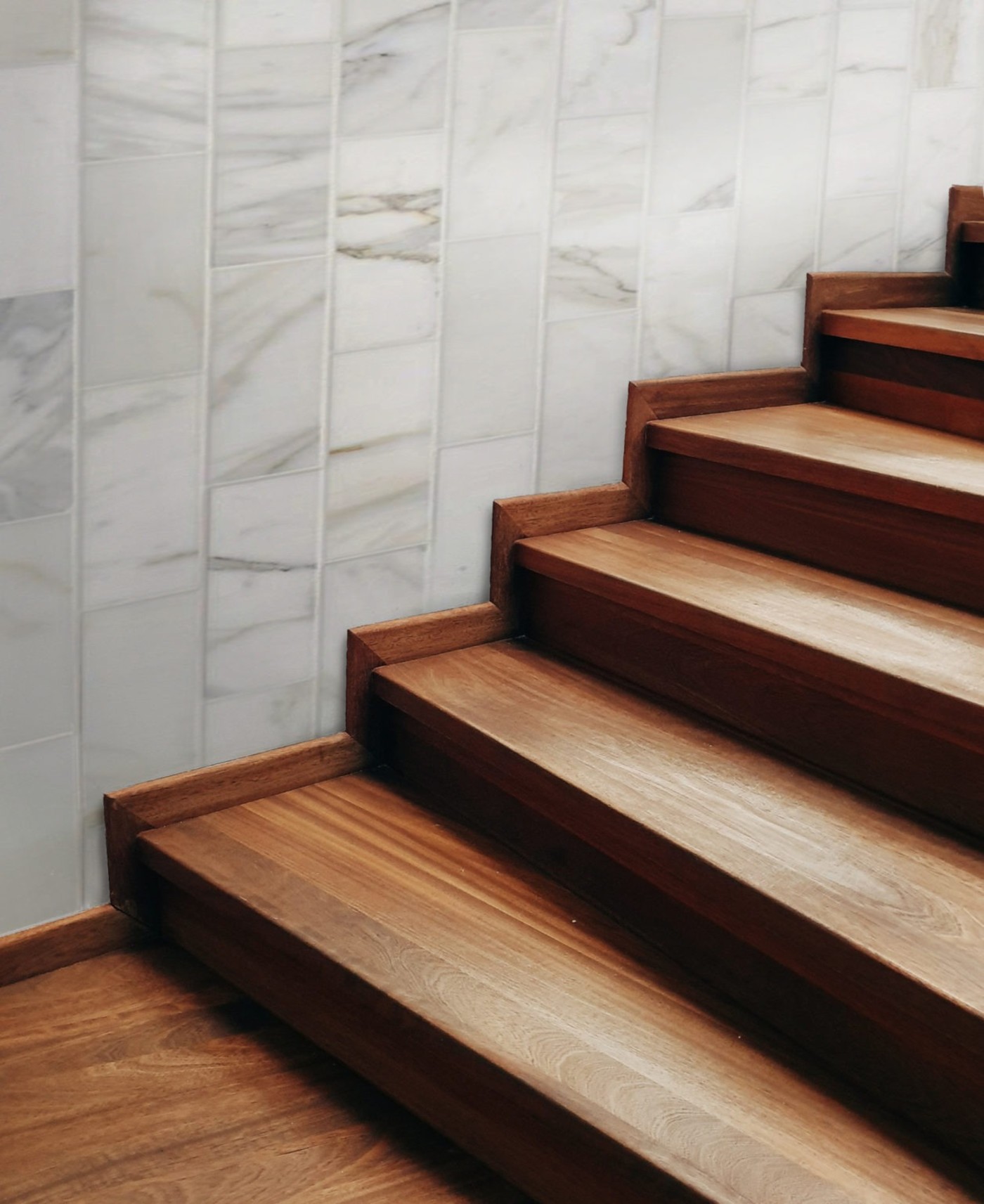 a wooden staircase next to a white tiled wall.