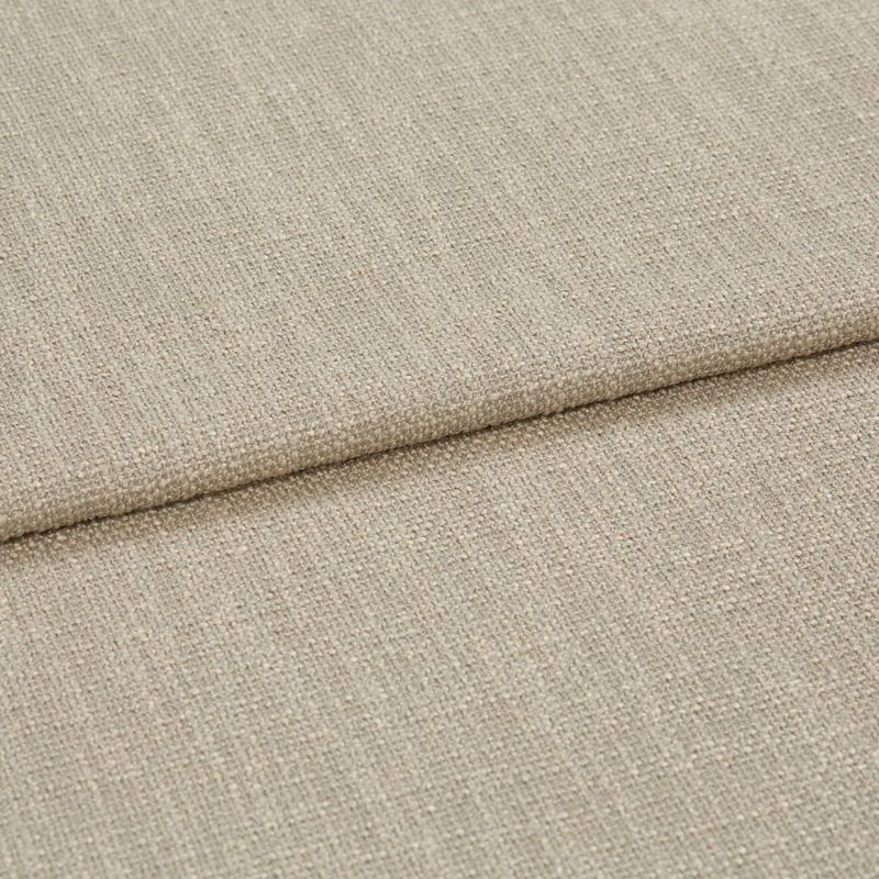 Beige woven fabric folded into overlapping panels, showing coarse textured upholstery weave; a horizontal fold/edge across frame, close-up studio-lit view suggesting a sofa cushion or fabric sample.