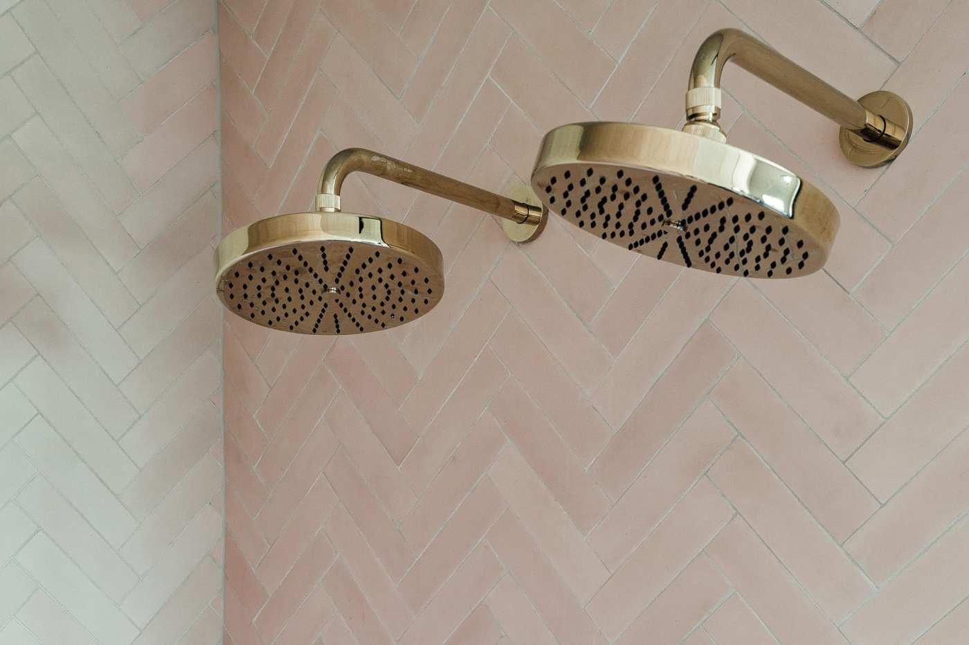 two brass shower heads on a pink tiled wall.