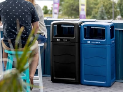 black and blue waste and recyclables bins made from 100% PCR material outdoors at patio bar with people sitting at table