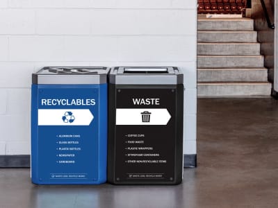 double waste and recycling bins sitting side by side with full body signs and brushed pewter lids in a sports stadium