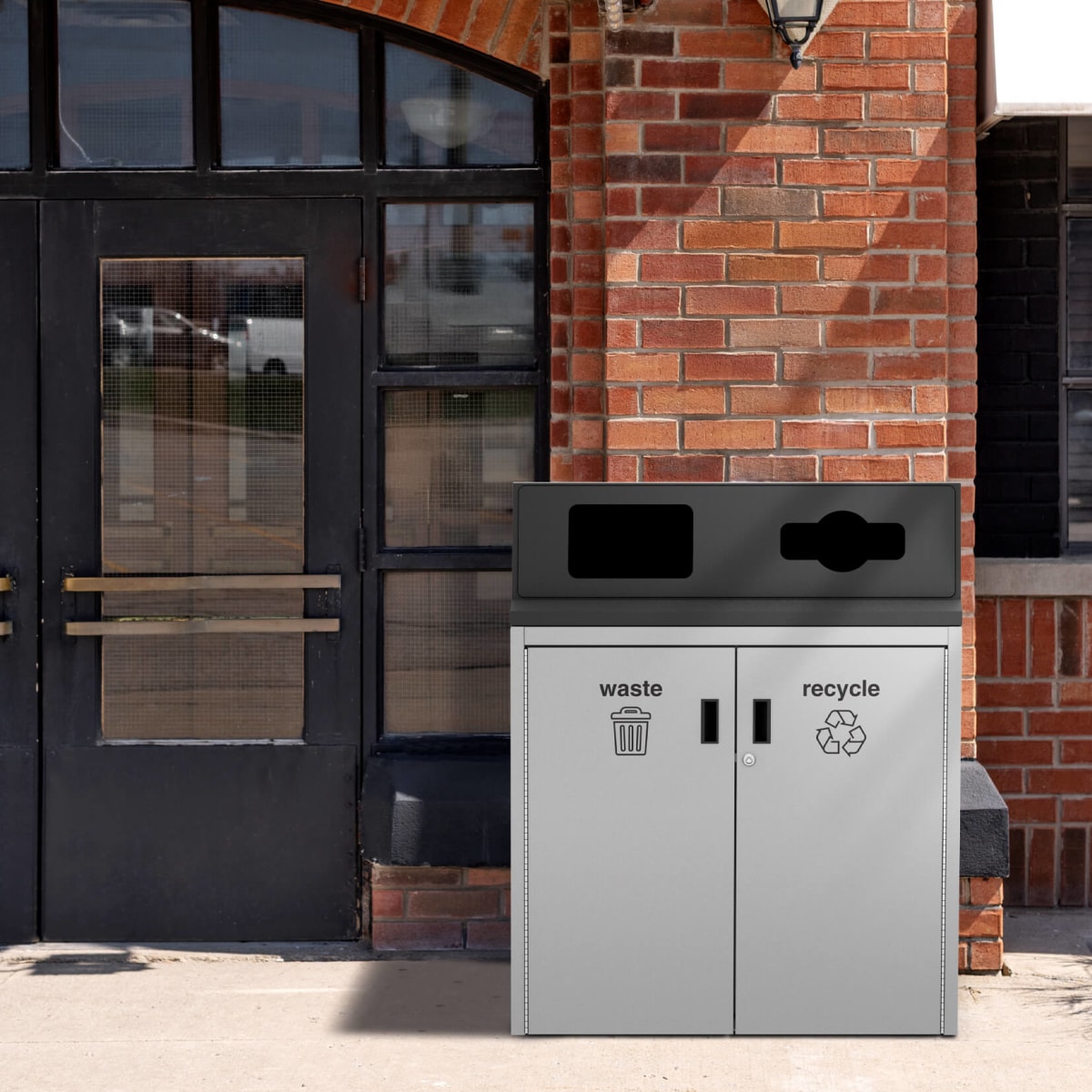 grey and black all metal trash and recyclables bin sitting at the entrance of a restaurant with red bricks