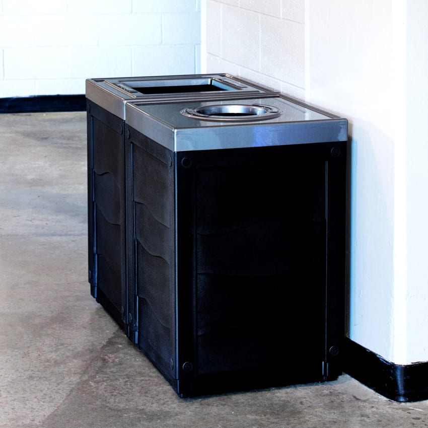 double waste and cans and bottles bins with black bodies against a wall in the hallway of an arena