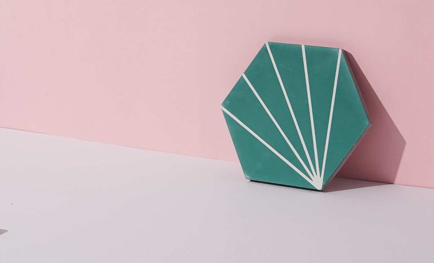 a green and white tile leaning against a wall on a pink surface.