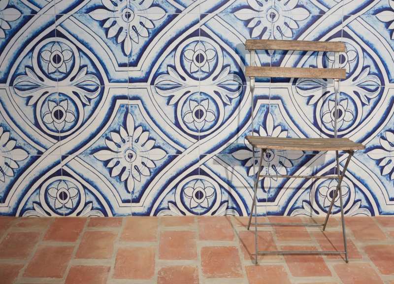 a room with a blue and white tiled wall, red tiled floor, and a wooden chair.