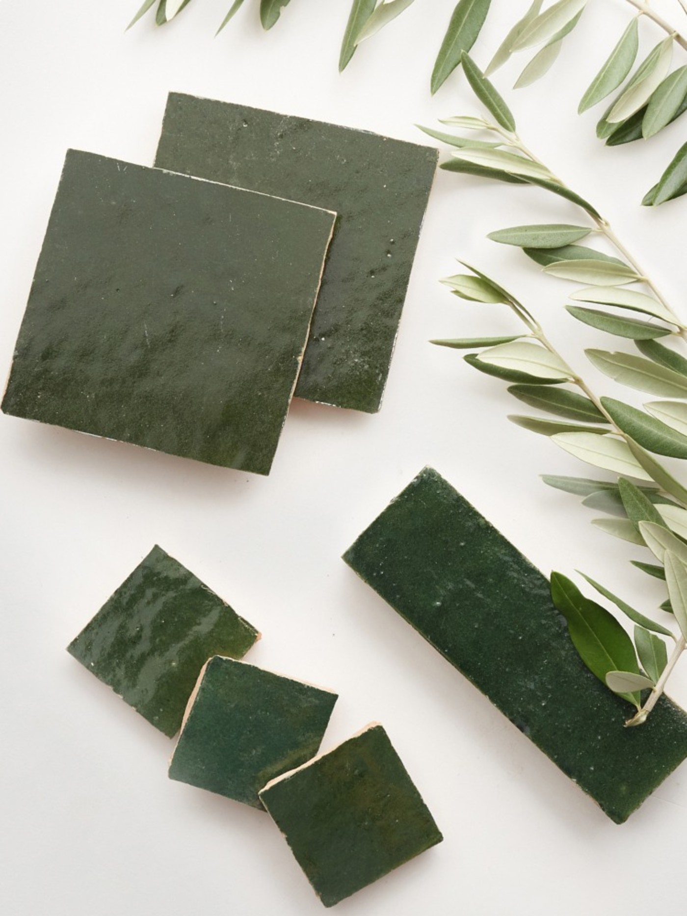 a set of green tiles arranged with olive leaves on a white surface.