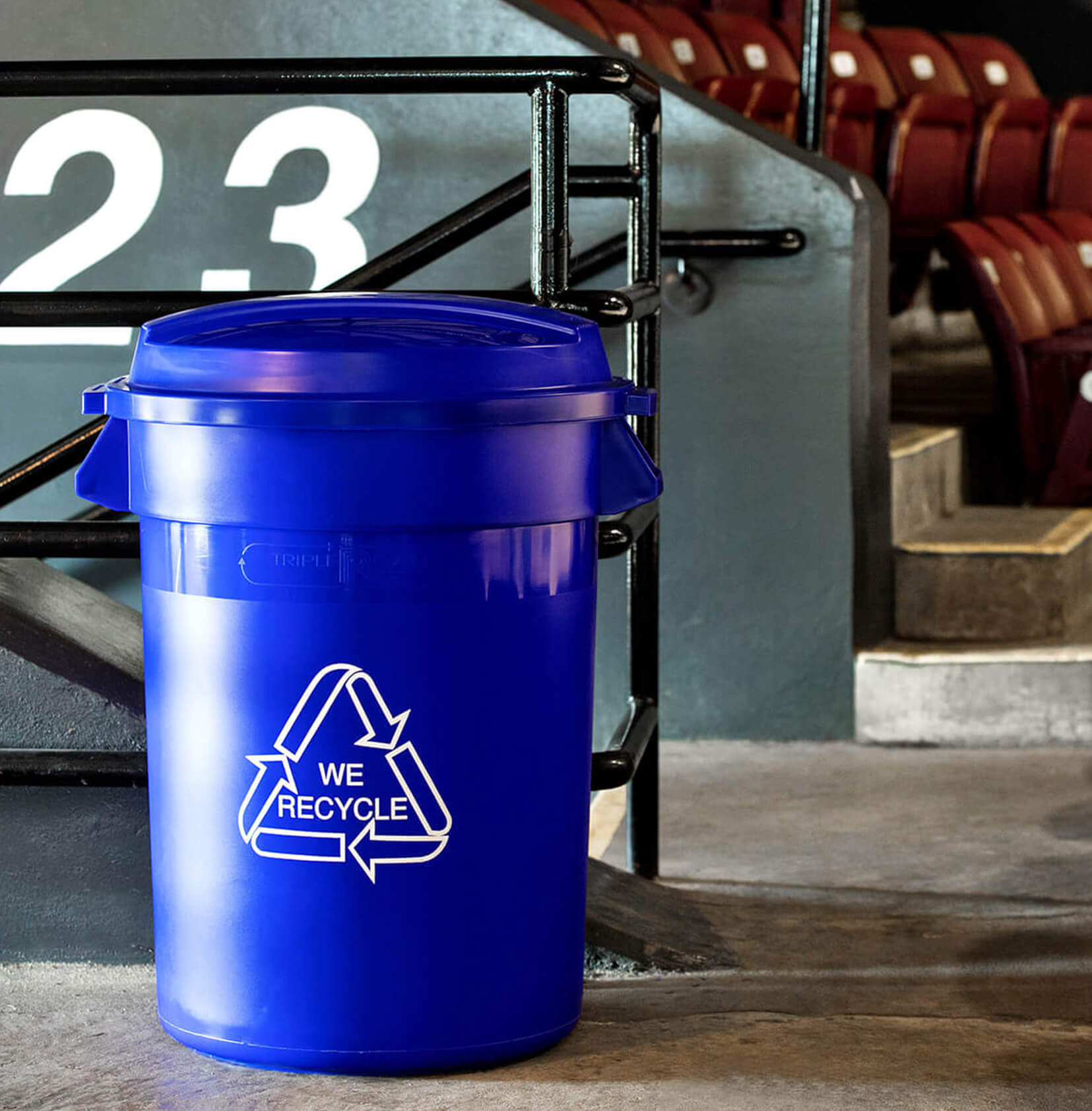 big capacity recycling container with we recycle printed on the side in a sports stadium