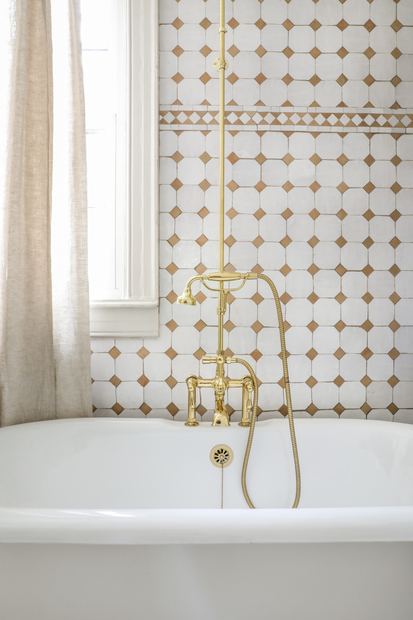 a bathtub with a gold faucet against a white and gold tiled wall.