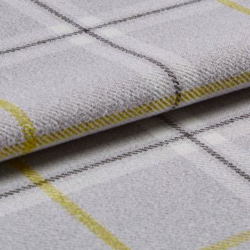 Woven plaid fabric folded to expose its edge and texture; close-up on a pale gray surface with thin yellow and dark grid lines, soft even studio lighting.