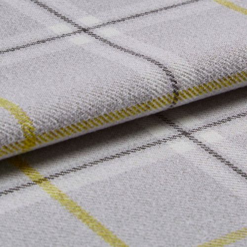 Woven plaid fabric folded to expose its edge and texture; close-up on a pale gray surface with thin yellow and dark grid lines, soft even studio lighting.