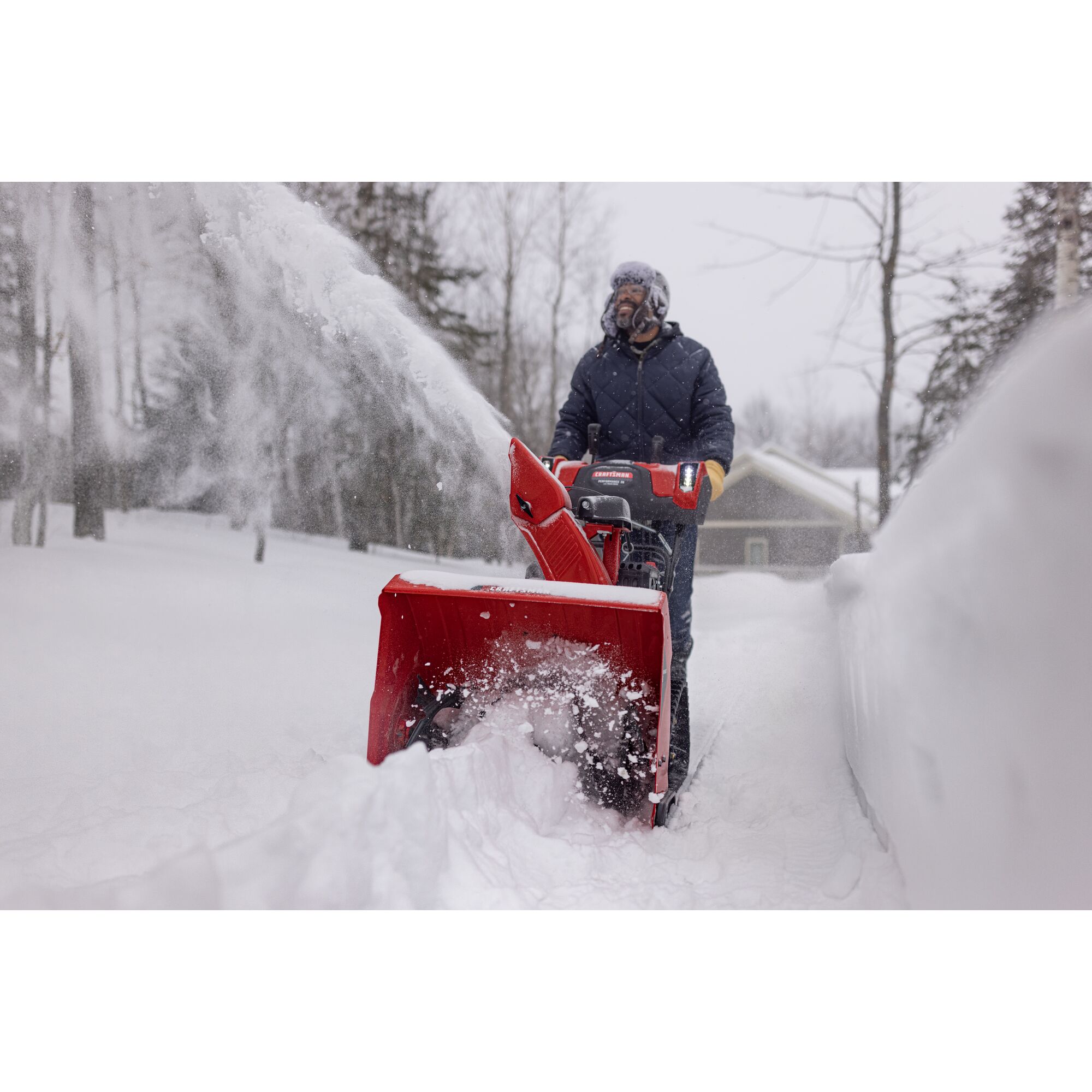 CRAFTSMAN Performance 26 Track Gas Snow Blower clearing snow with trees and house in background