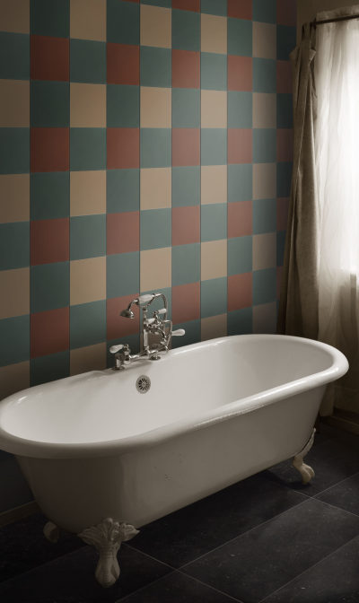 a bathtub in a bathroom with a tricolored checkered tile wall.