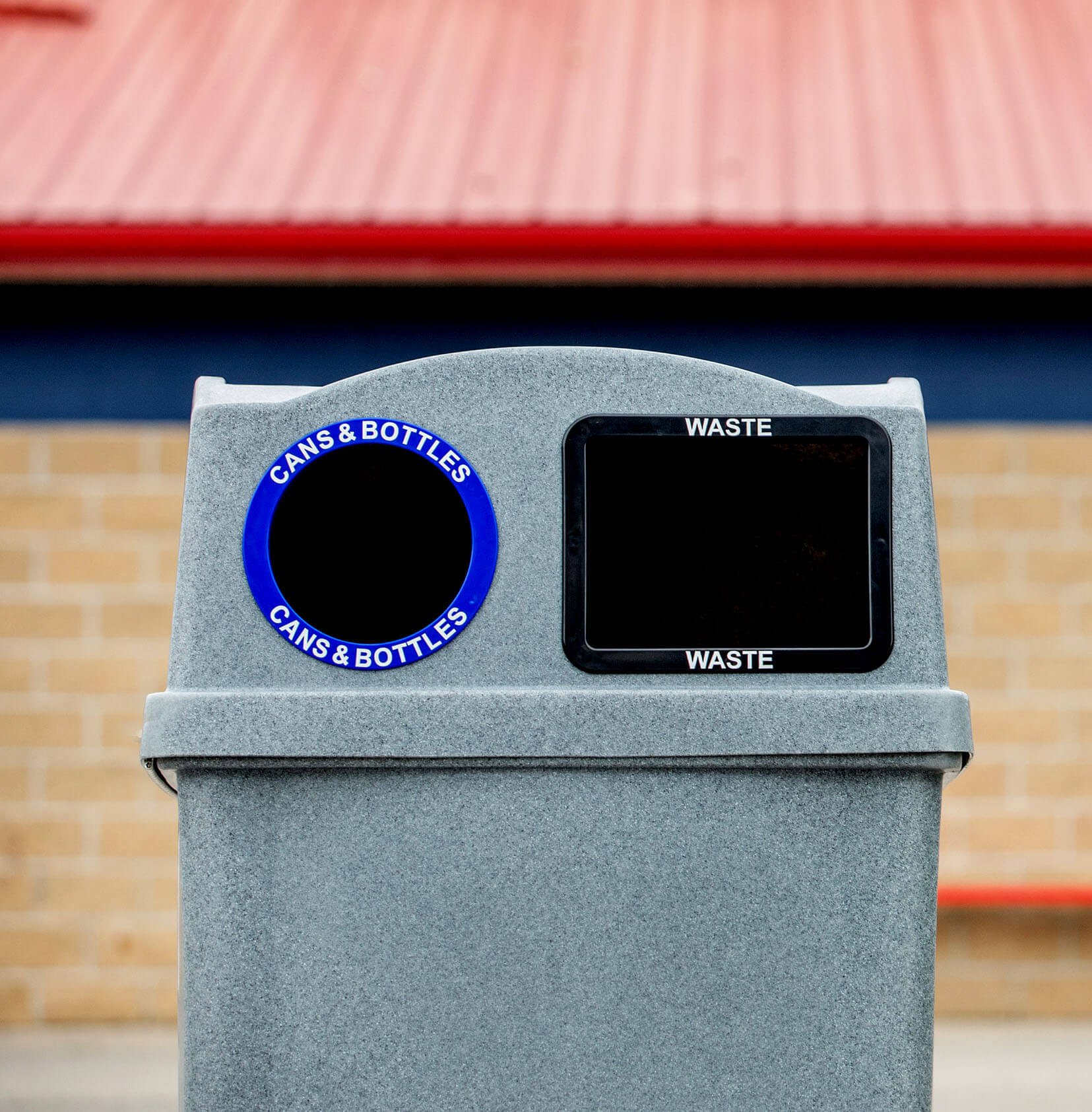 closeup of a waste and recycling bin with color-coded restrictive openings at a sports field