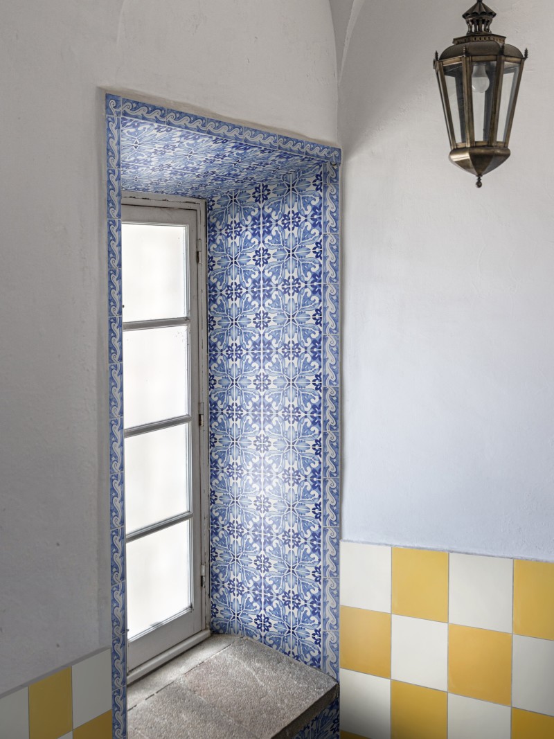 a window surrounded by blue and white tiled walls in a room with a yellow and white checkered floor.