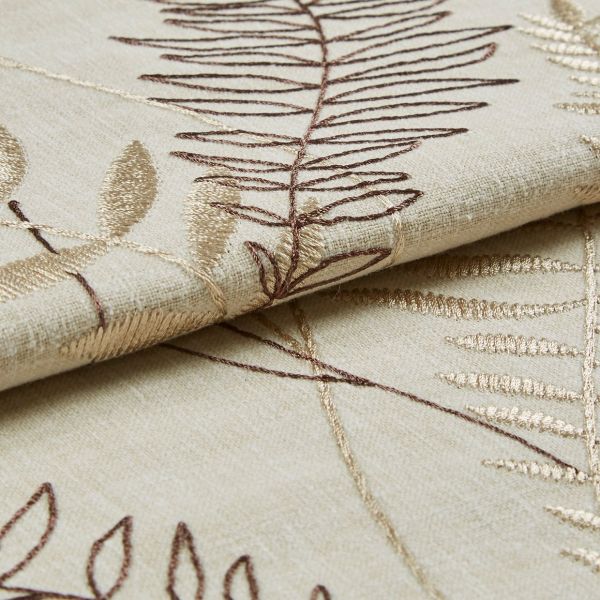 Beige embroidered curtain fabric, folded to show overlapping panels with brown and gold leaf-stitch motifs; embroidery raised and textured; close-up studio shot with soft, even lighting on a neutral surface.