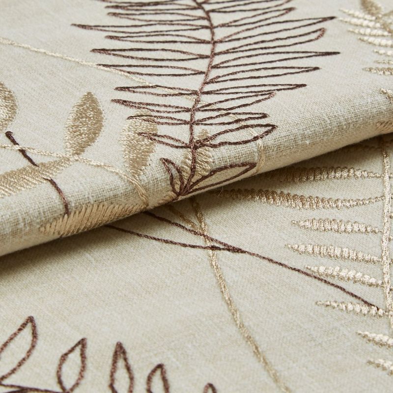 Beige embroidered curtain fabric, folded to show overlapping panels with brown and gold leaf-stitch motifs; embroidery raised and textured; close-up studio shot with soft, even lighting on a neutral surface.