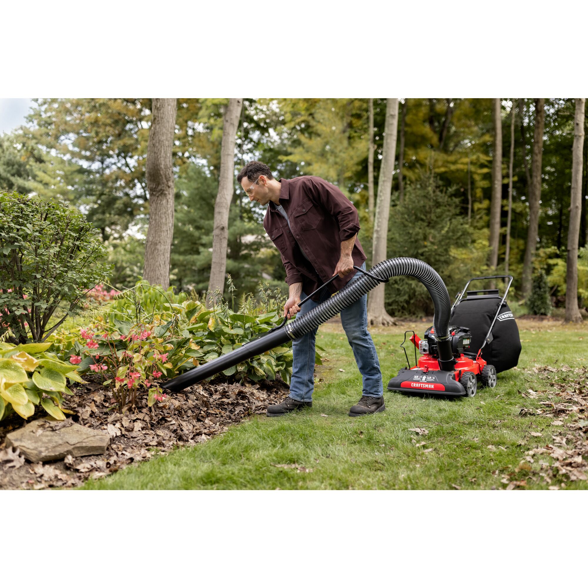 CRAFTSMAN 24-In. 163cc Chipper Shredder Vacuum attached to mower using hand vacuum removing leaves in flowerbed
