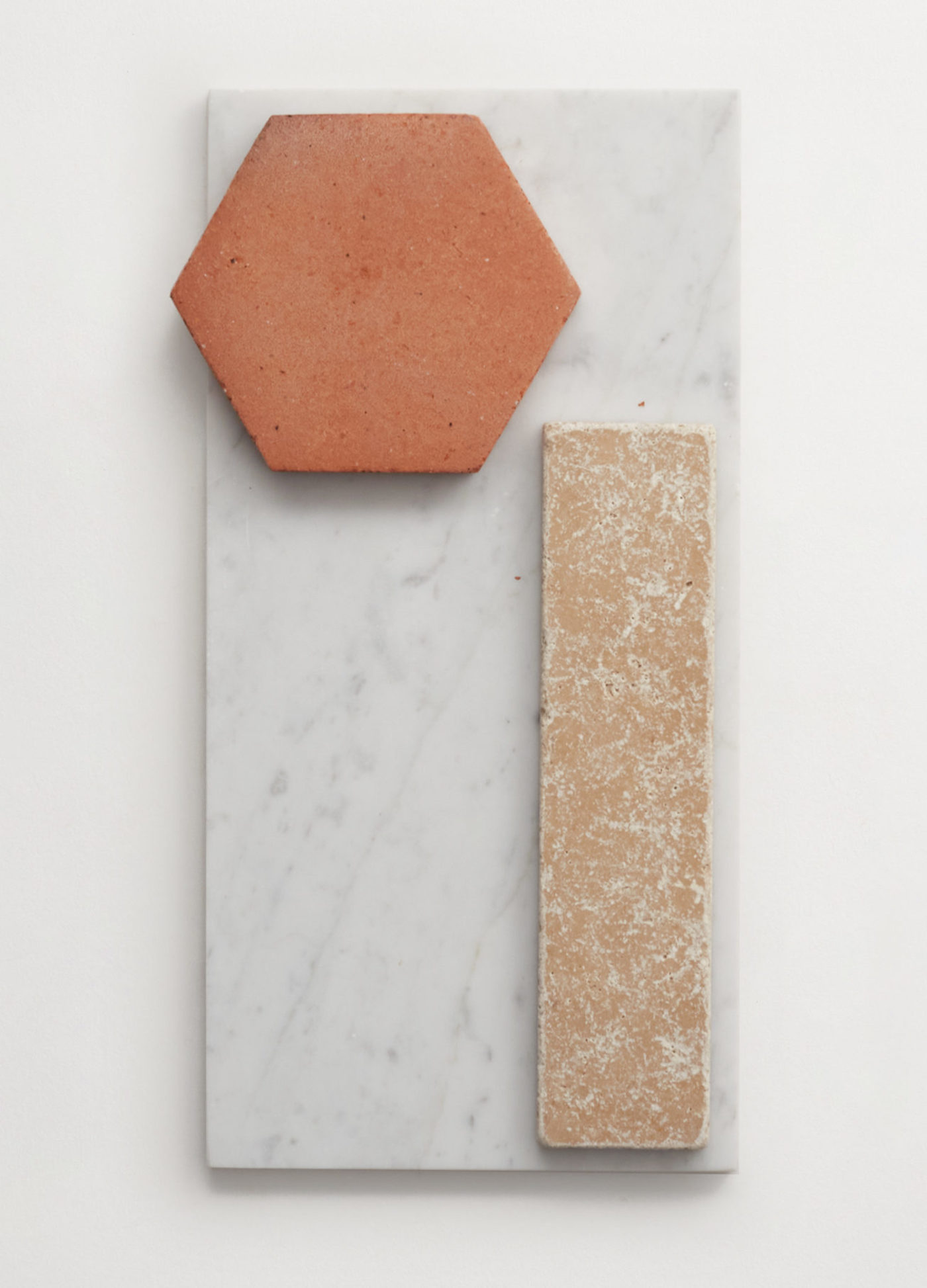 a red terracotta hex tile, rectangular marble tile and rectangular stone tile on a white surface.