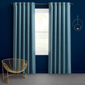 Teal grommet-top curtains, full-length panels on a metal rod, drawn slightly apart and filtering light from a window; navy-painted room with gray carpet, brass wire chair and circular wall sconce.