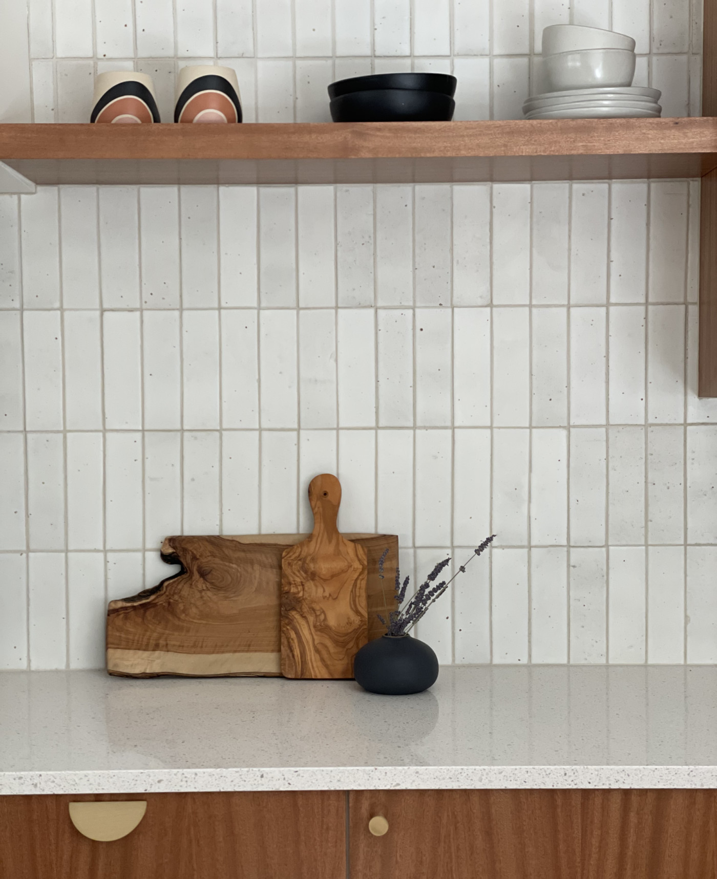 a white kitchen with wooden shelves and a wooden cutting board.