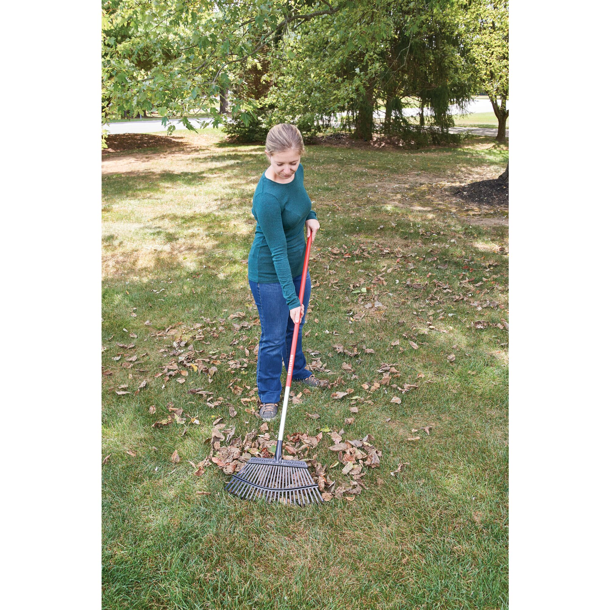 25 tine aluminum handle lawn rake being used by a person to rake leaves from the ground.