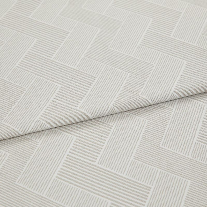 Cream textured fabric with raised linear herringbone rectangles, folded and overlapping across the frame, showing ribbed weave detail in a close-up product shot with soft, diffuse lighting.