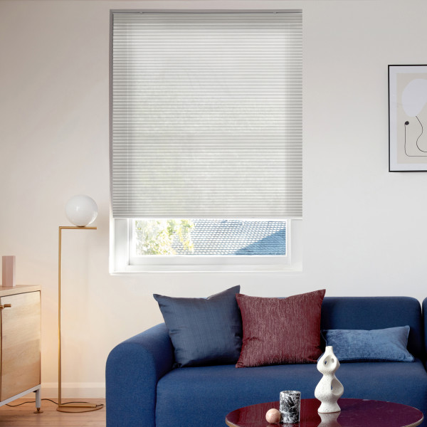 White cellular pleated blind lowered across window, translucent and filtering soft daylight; small modern living room with blue sofa, textured cushions, brass floor lamp, coffee table and framed abstract art.
