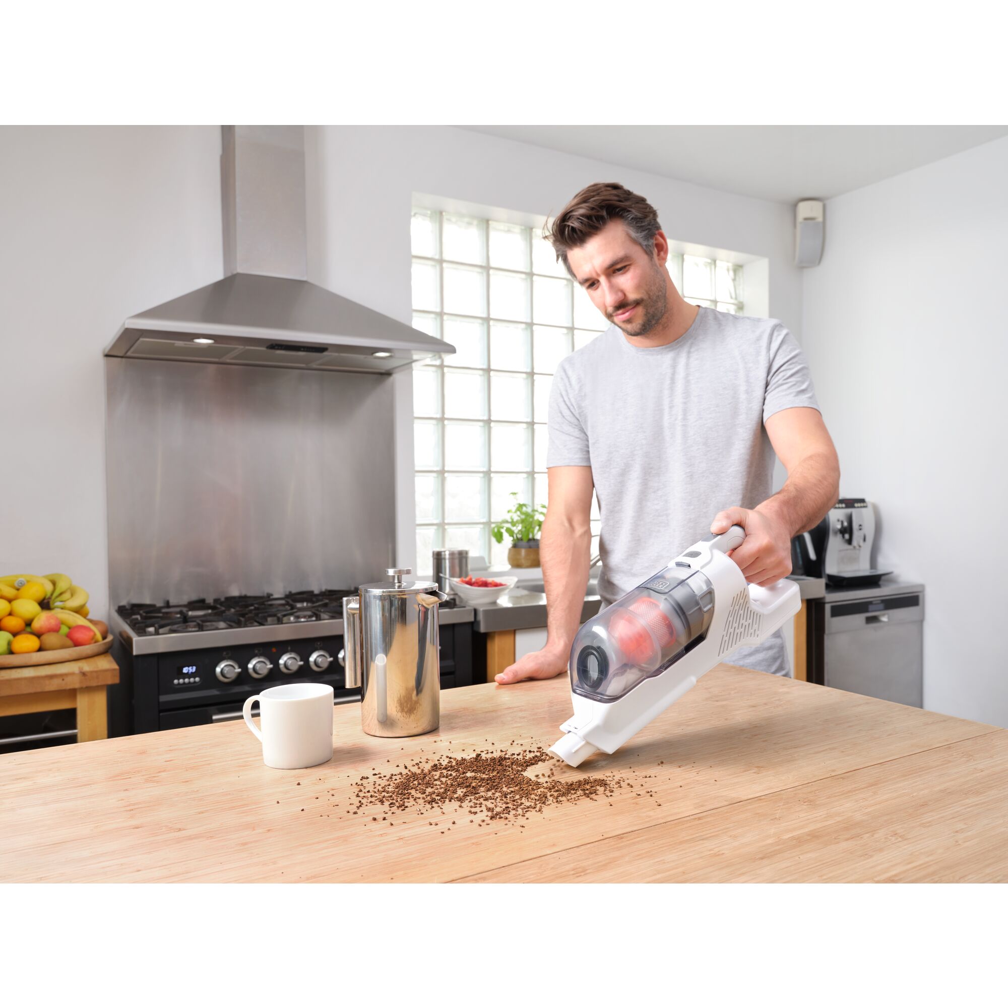 Handheld portion of Black and decker power series plus cordless stick vacuum being used by person to clean up spilled coffee grounds on a countertop