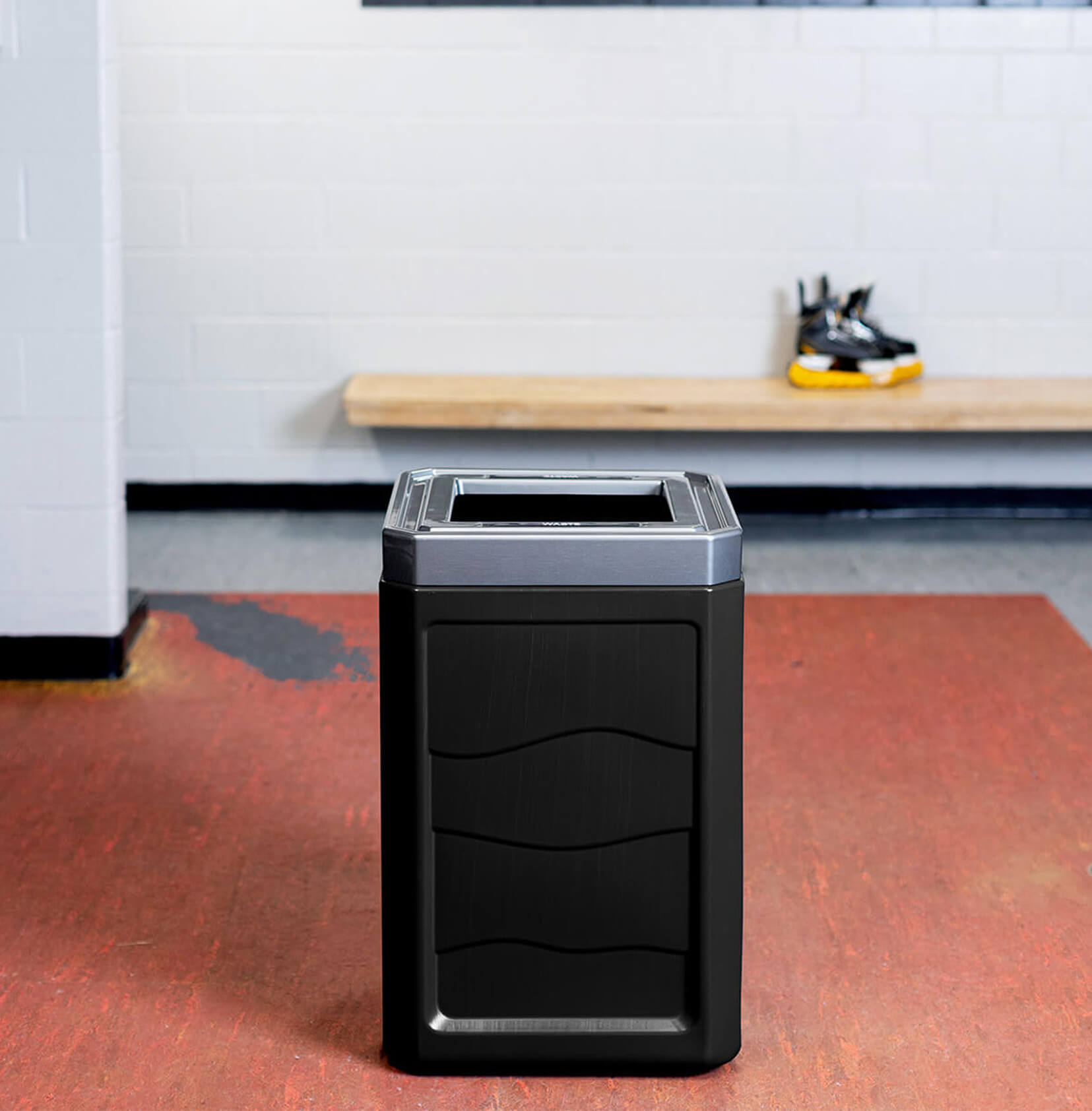 large trash container made from durable 100% recycled plastic body with a stainless steel looking lid inside a hockey locker room