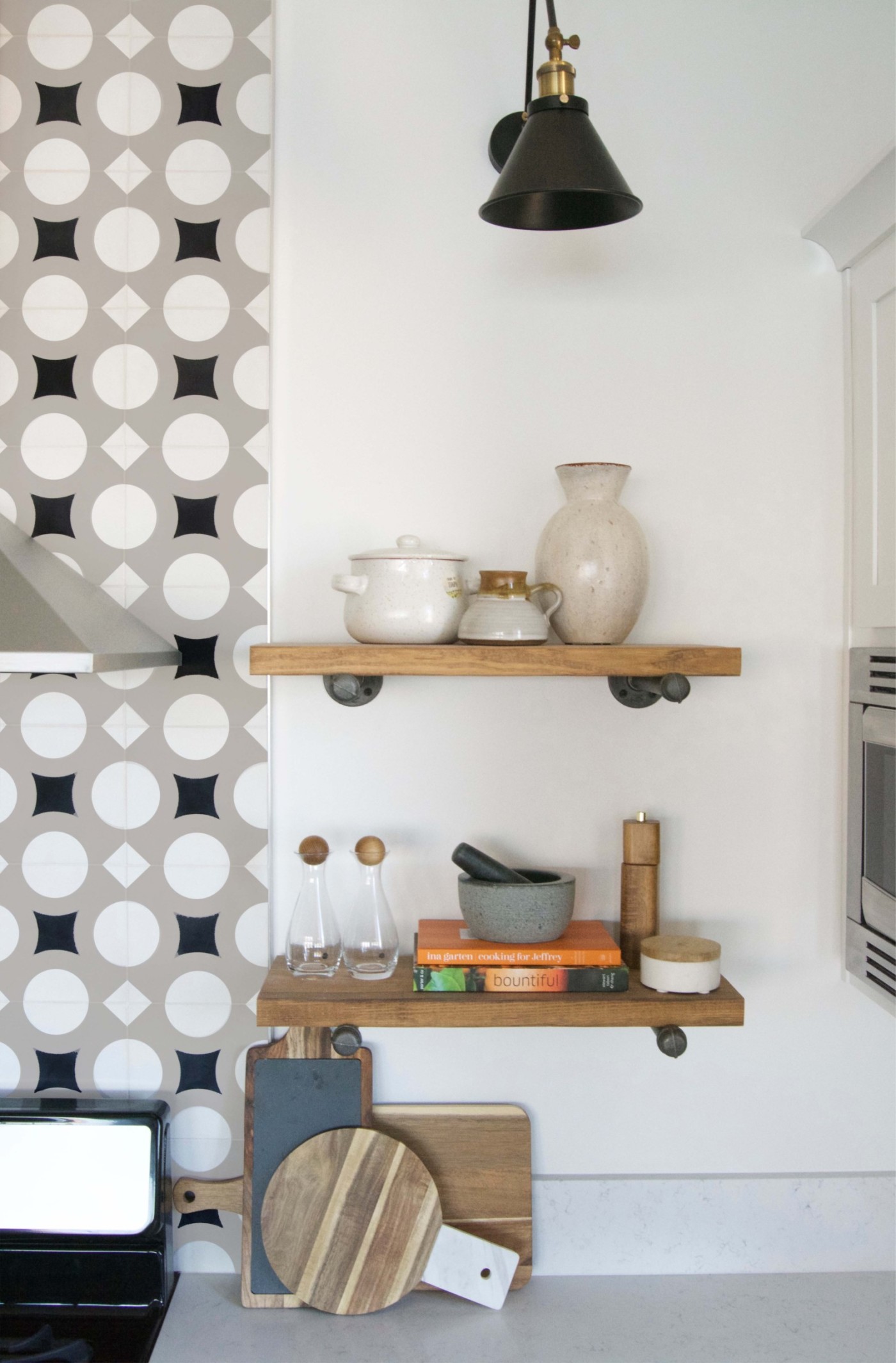 a kitchen with a wooden shelf and a black and white tiled wall.