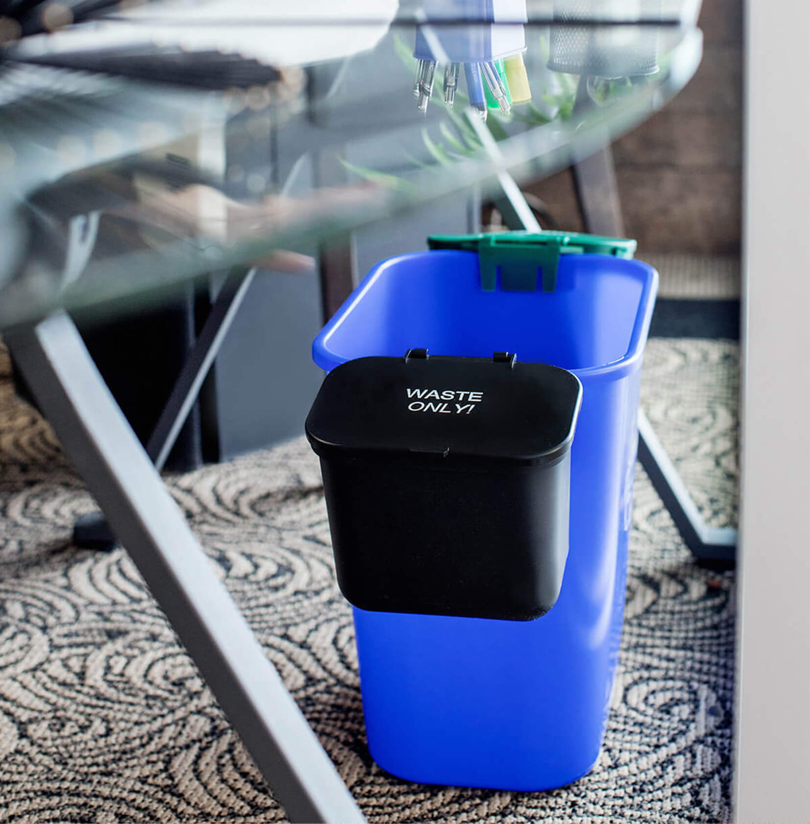 blue recycling bin with two hanging waste and organics collection bins on each side sitting under a modern desk in an office