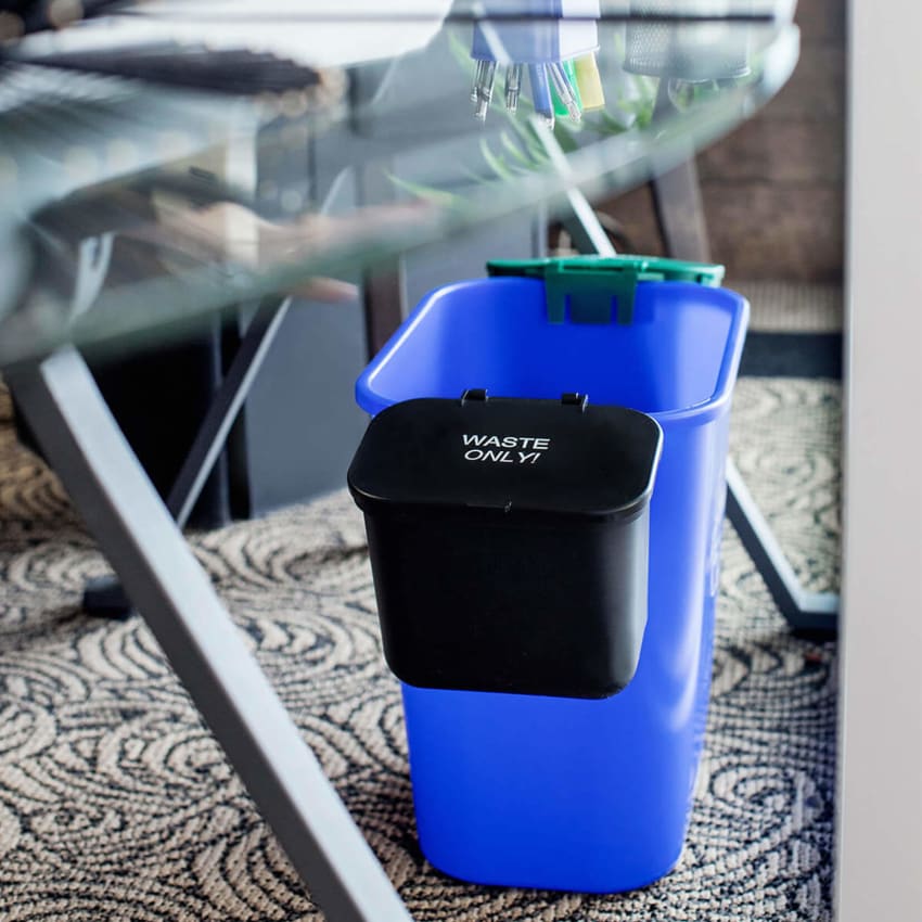 blue recycling bin with two hanging waste and organics collection bins on each side sitting under a modern desk in an office