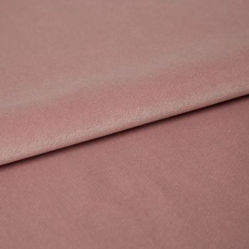 Dusty-rose velvet fabric folded across the frame, overlapping with a visible crease; its nap catches soft highlights in a close-up studio view on a flat surface.