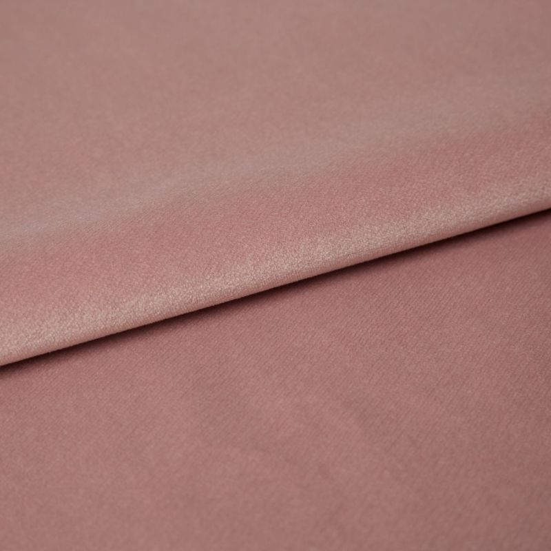 Dusty-rose velvet fabric folded across the frame, overlapping with a visible crease; its nap catches soft highlights in a close-up studio view on a flat surface.