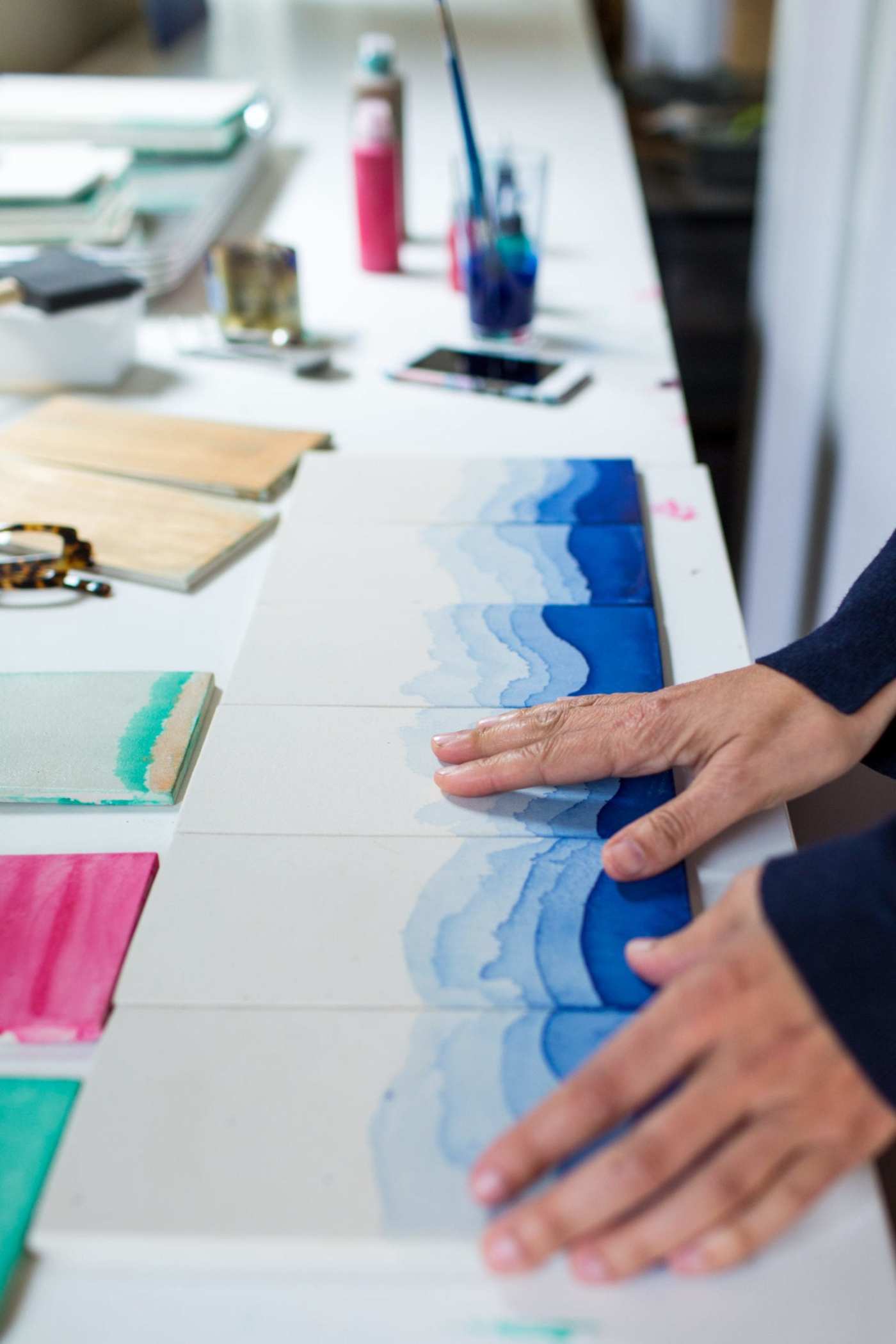 a woman's hands touching blue and white patterned tiles on a table.