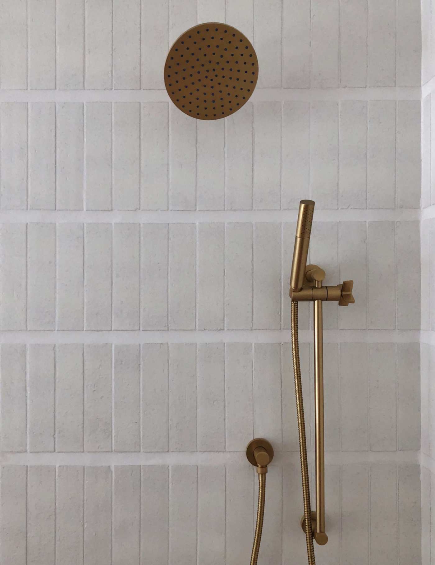 a brass shower head and handle in a white tiled shower.