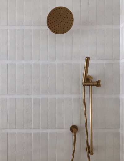 a shower head with a brass handle and a white tiled wall.
