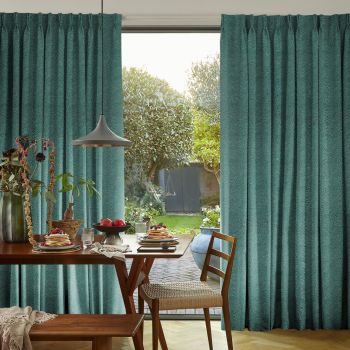 Teal textured curtains, hung to the sides and pulled open, framing an open door revealing a sunlit garden; wooden dining table set for breakfast with pancakes, fruit, and a pendant lamp.