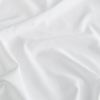 White satin fabric spread across a surface, rumpled into gentle folds and creases that catch soft diffuse light, close-up view with a neutral background.