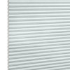 Pleated honeycomb blind, pale gray-blue with hexagonal cells along the left edge, fully lowered and closed, softly filtering daylight, set against a bright white background in a neutral-lit interior.