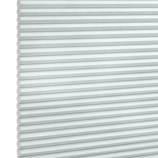 Pleated honeycomb blind, pale gray-blue with hexagonal cells along the left edge, fully lowered and closed, softly filtering daylight, set against a bright white background in a neutral-lit interior.