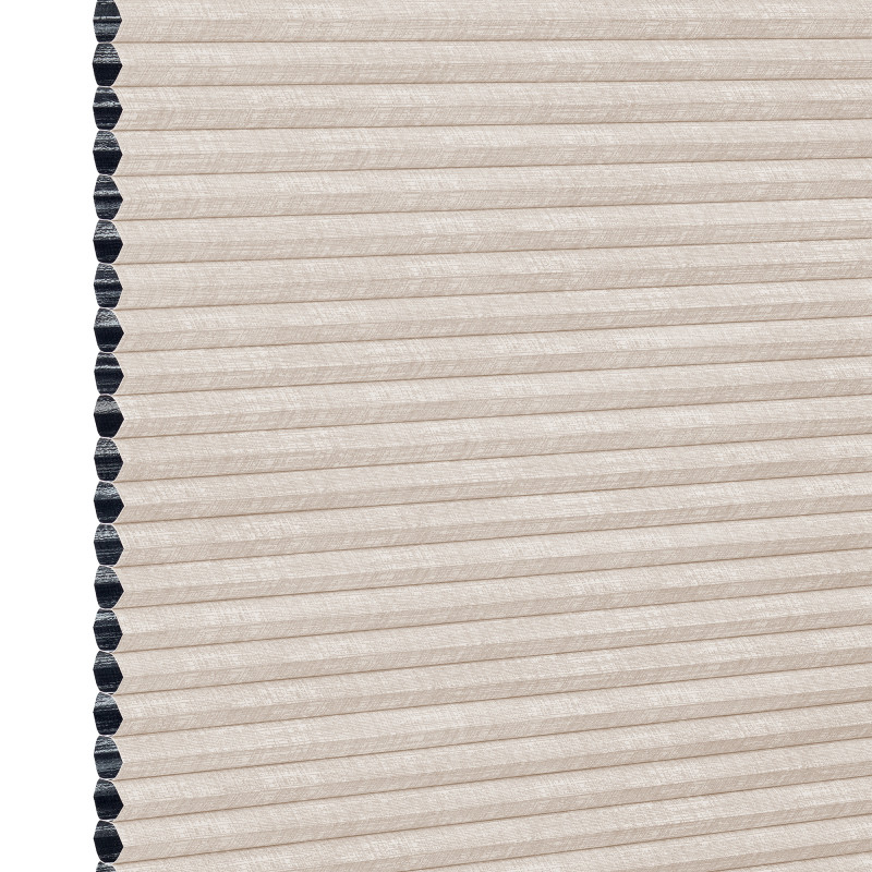 Beige cellular (honeycomb) window shade, pleated and fully lowered with exposed black cell openings along the left edge, blocking light and showing a textured fabric surface against a white background.