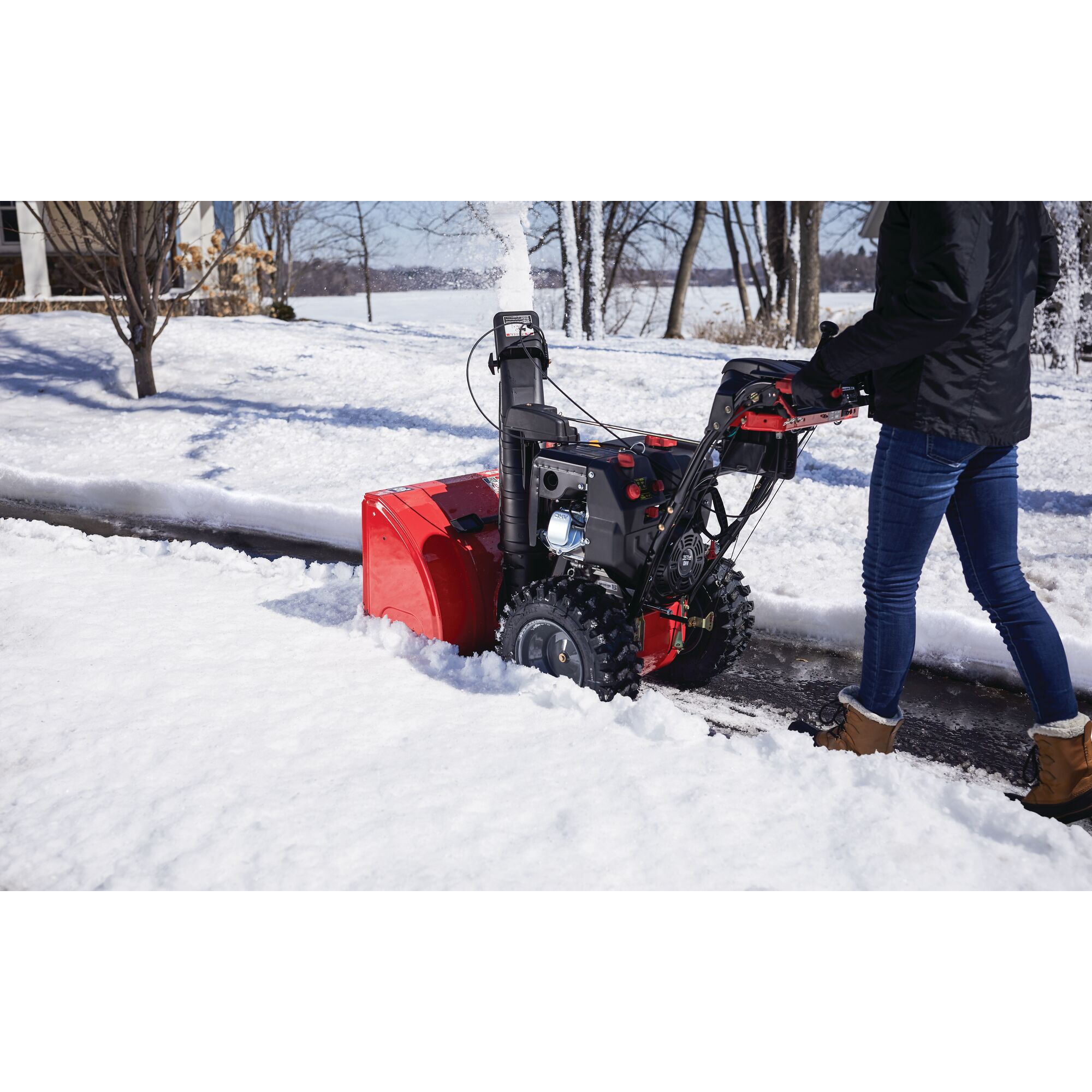 CRAFTSMAN Electric Start Two-Stage Snow Blower in left side view blowing snow in driveway wearing black jacket