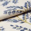 Cream woven curtain fabric with raised blue floral motifs and gold-thread stems â€” folded and layered, showing textured weave â€” close-up studio-lit textile sample with soft, neutral background.