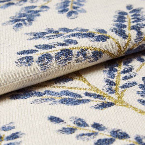 Cream woven curtain fabric with raised blue floral motifs and gold-thread stems — folded and layered, showing textured weave — close-up studio-lit textile sample with soft, neutral background.