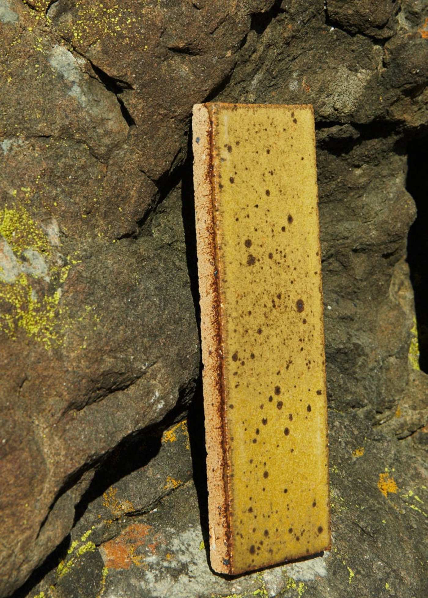 a yellow rectangular tile sitting on top of a rock.